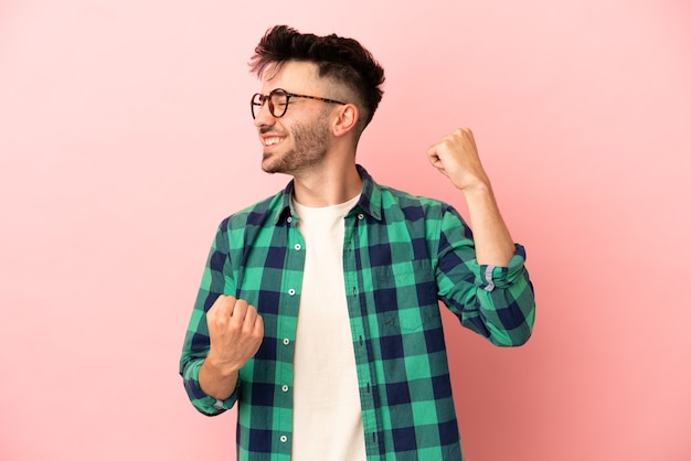 Giovane uomo caucasico isolato su sfondo rosa che celebra una vittoria