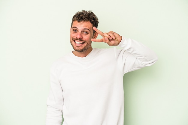 Giovane uomo caucasico isolato su sfondo verde ballare e divertirsi.