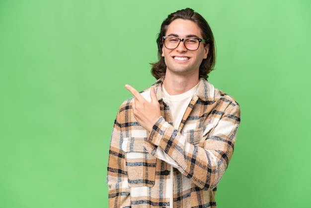 Giovane uomo caucasico isolato su sfondo verde croma che indica il lato per presentare un prodotto