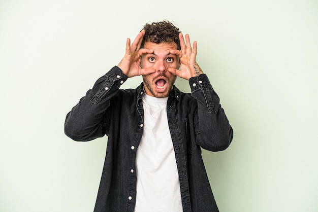 Giovane uomo caucasico isolato su sfondo verde tenendo gli occhi aperti per trovare un'opportunità di successo.