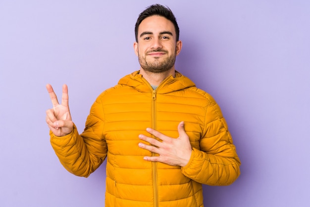 Giovane uomo caucasico isolato su viola prestando giuramento, mettendo la mano sul petto.