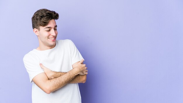 Giovane uomo caucasico isolato su viola sorridente fiducioso con le braccia incrociate.