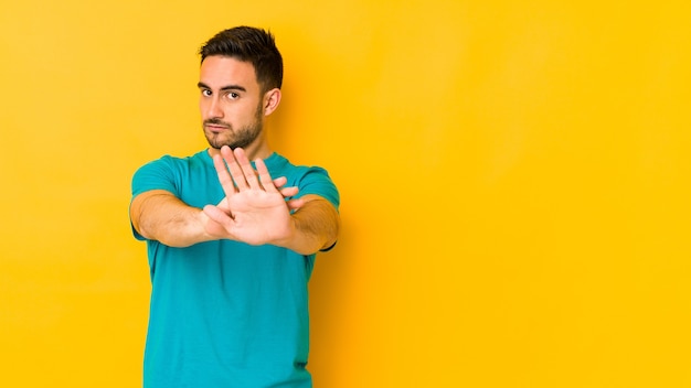 Giovane uomo caucasico isolato sul muro giallo in piedi con la mano tesa che mostra il segnale di stop, impedendoti.