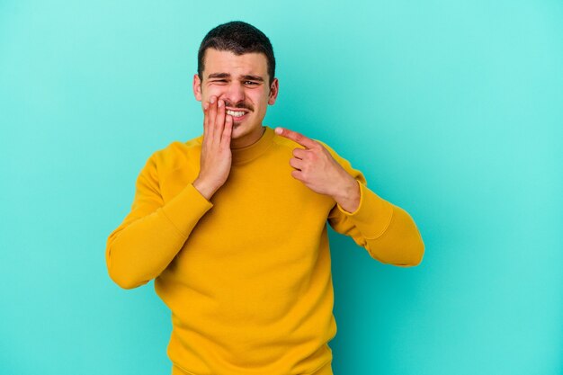 Giovane uomo caucasico isolato sulla parete blu con un forte dolore ai denti, dolore molare.