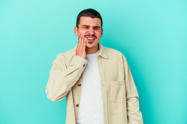 Giovane uomo caucasico isolato sulla parete blu con un forte dolore ai denti, dolore molare.