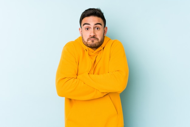 Giovane uomo caucasico isolato sulle spalle di scrollate di spalle blu e gli occhi aperti confusi.