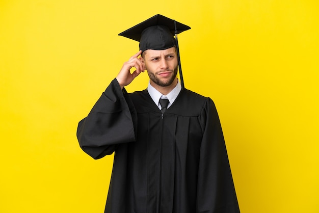 Giovane uomo caucasico laureato isolato su sfondo giallo che ha dubbi e con un'espressione del viso confusa