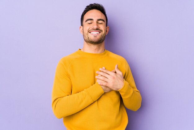 Giovane uomo caucasico ridendo mantenendo le mani sul cuore, il concetto di felicità.