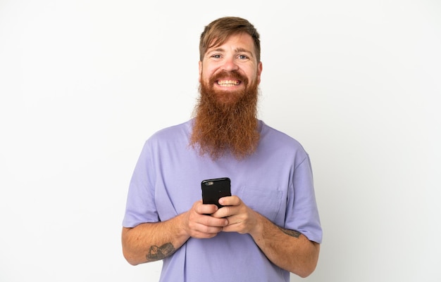 Giovane uomo caucasico rossastro isolato su sfondo bianco che invia un messaggio con il cellulare