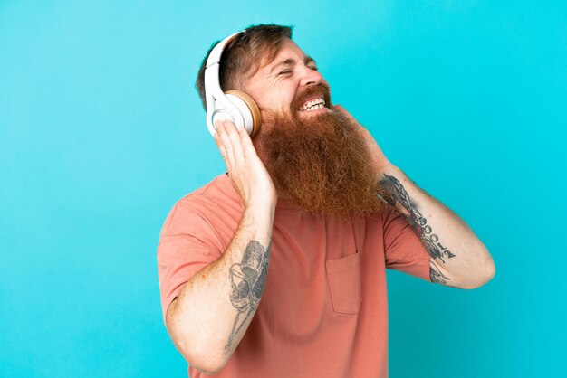 Giovane uomo caucasico rossastro isolato su sfondo blu ascoltando musica e cantando