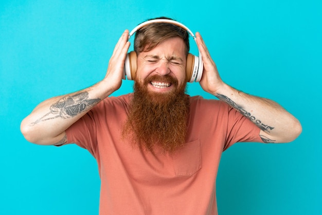 Giovane uomo caucasico rossastro isolato su sfondo blu ascoltando musica