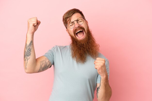 Giovane uomo caucasico rossastro isolato su sfondo rosa che celebra una vittoria