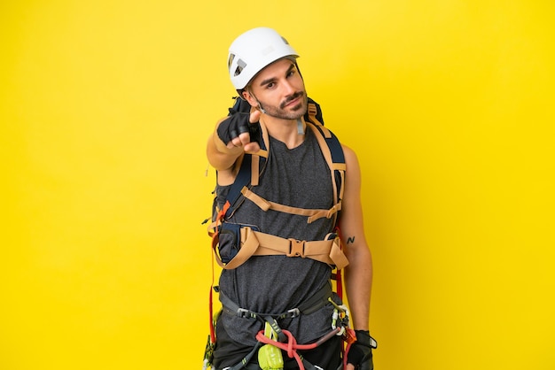 Giovane uomo caucasico scalatore di roccia isolato su sfondo giallo punta il dito contro di te con un'espressione sicura