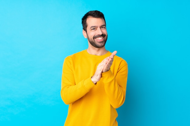 Giovane uomo caucasico sopra la parete blu isolata che applaude dopo la presentazione in una conferenza