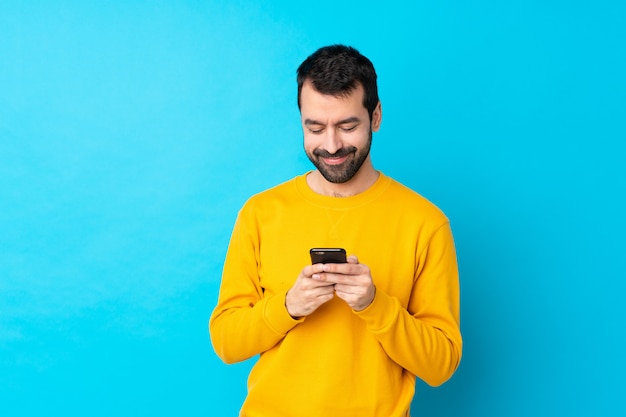 Giovane uomo caucasico sopra la parete blu isolata che invia un messaggio con il cellulare
