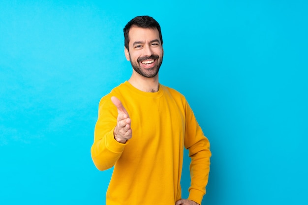 Giovane uomo caucasico sopra la parete blu isolata che stringe le mani per la chiusura molto