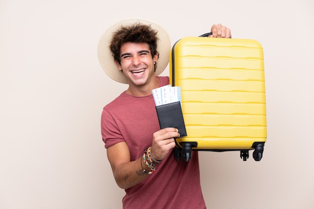Giovane uomo caucasico sopra la parete isolata in vacanza con la valigia e il passaporto
