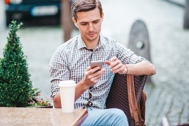 Giovane uomo caucasico sorridente felice utilizzando smartphone all'aperto