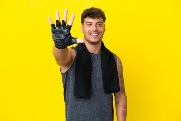 Giovane uomo caucasico sportivo con asciugamano isolato su sfondo giallo contando cinque con le dita