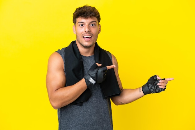 Giovane uomo caucasico sportivo con asciugamano isolato su sfondo giallo sorpreso e indicando il lato