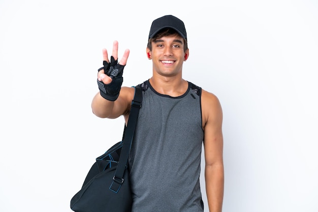 Giovane uomo caucasico sportivo con borsa sportiva isolata su sfondo bianco felice e contando tre con le dita