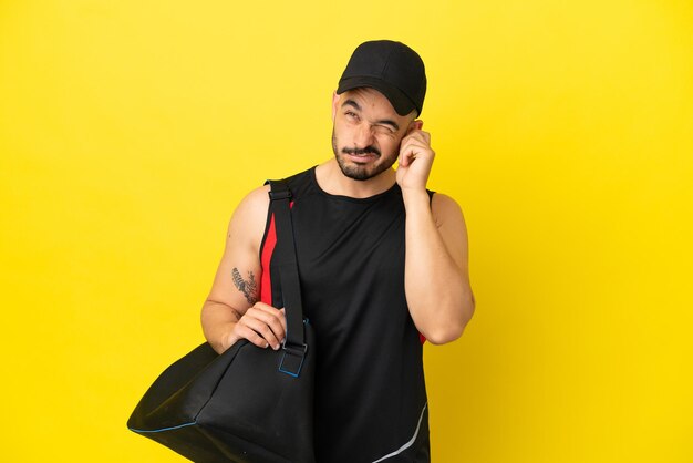 Giovane uomo caucasico sportivo con borsa sportiva isolato su sfondo giallo frustrato e che copre le orecchie