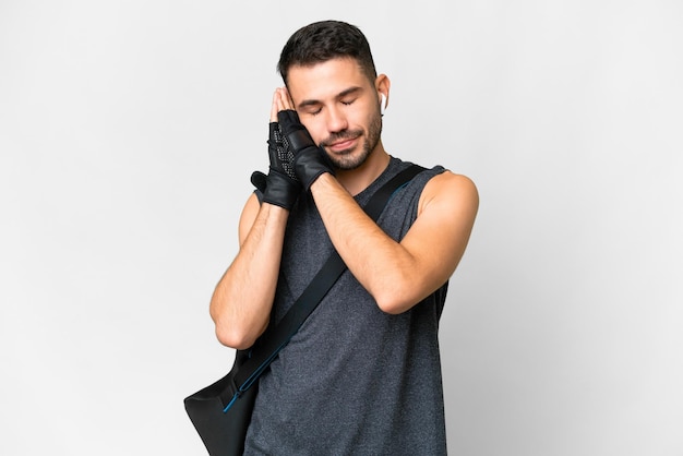 Giovane uomo caucasico sportivo con borsa sportiva su sfondo bianco isolato che fa il gesto del sonno in un'espressione adorabile