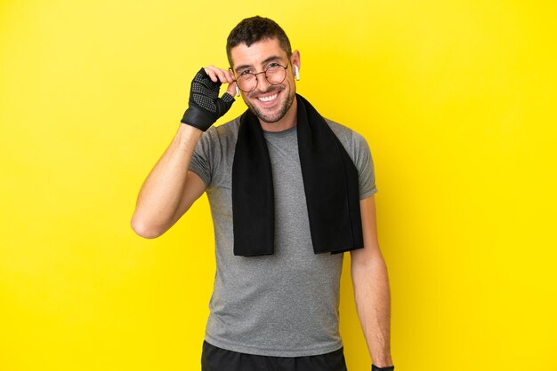 Giovane uomo caucasico sportivo isolato su sfondo giallo con occhiali e felice