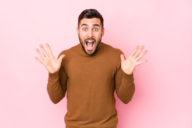 Giovane uomo caucasico su sfondo rosa isolato per celebrare una vittoria o un successo, è sorpreso e scioccato.