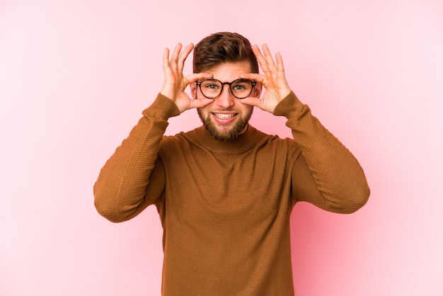 Giovane uomo caucasico sulla parete rosa tenendo gli occhi aperti