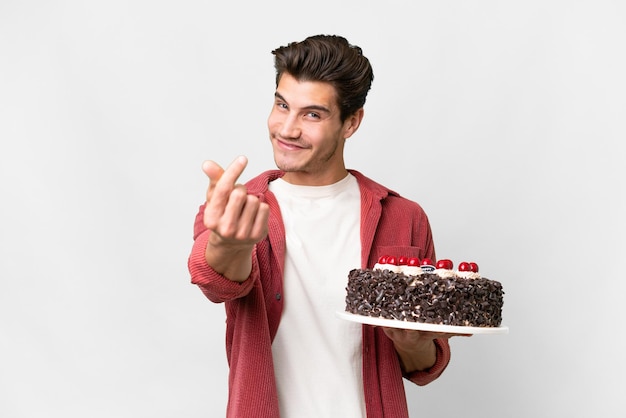 Giovane uomo caucasico tenendo la torta di compleanno su sfondo isolato facendo gesto di denaro