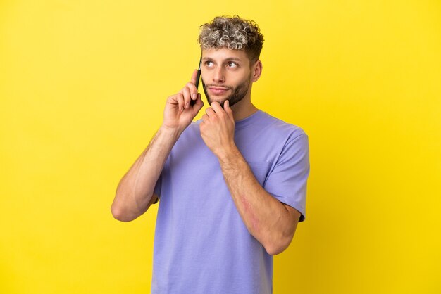 Giovane uomo caucasico utilizzando il telefono cellulare isolato su sfondo giallo e guardando in alto