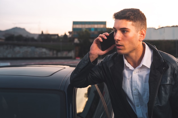 Giovane uomo caucasico utilizzando uno smartphone con un'auto sportiva dietro