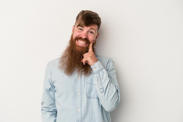 Giovane uomo caucasico zenzero con barba lunga isolato su sfondo bianco sorridente felice e sicuro di sé, toccando il mento con la mano.