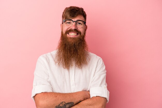 Giovane uomo caucasico zenzero con barba lunga isolato su sfondo rosa che si sente sicuro, incrociando le braccia con determinazione.