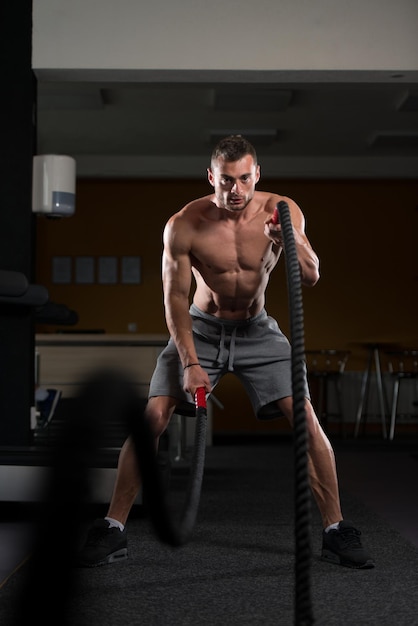 Giovane uomo che combatte le corde all'esercizio di allenamento in palestra