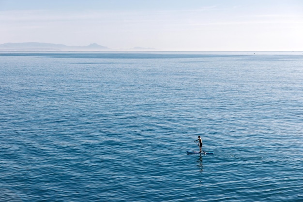 Giovane uomo che galleggia su una tavola SUP L'avventura del mare con acqua blu su un surf