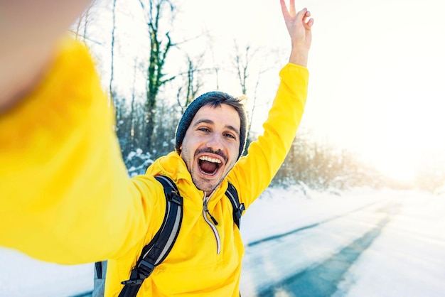 Giovane uomo che indossa abiti invernali che scatta foto selfie nella foresta di neve invernale