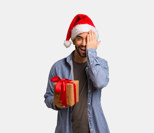 Giovane uomo che indossa cappello santa gridando felice e coprendo il viso con la mano