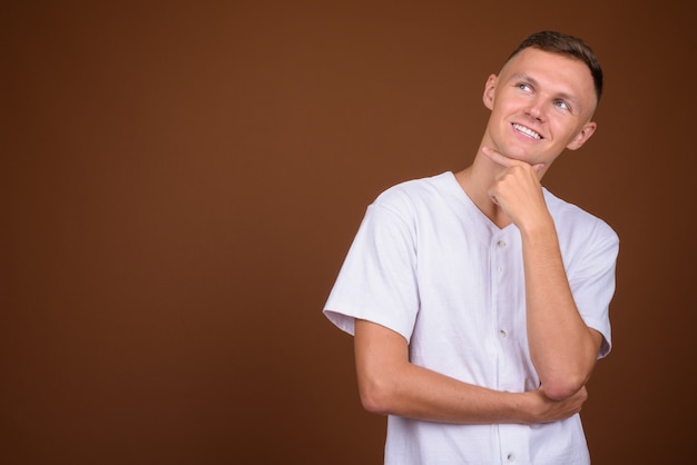 Giovane uomo che indossa una camicia bianca su sfondo marrone