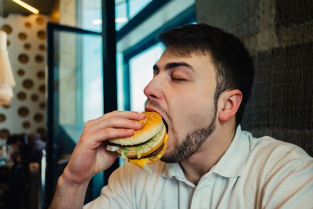 Giovane uomo che mangia un hamburger in un ristorante