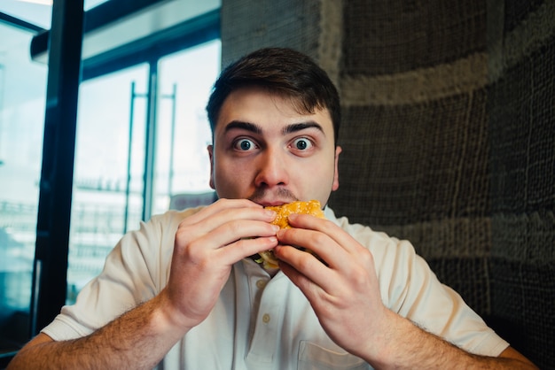 Giovane uomo che mangia un hamburger in un ristorante