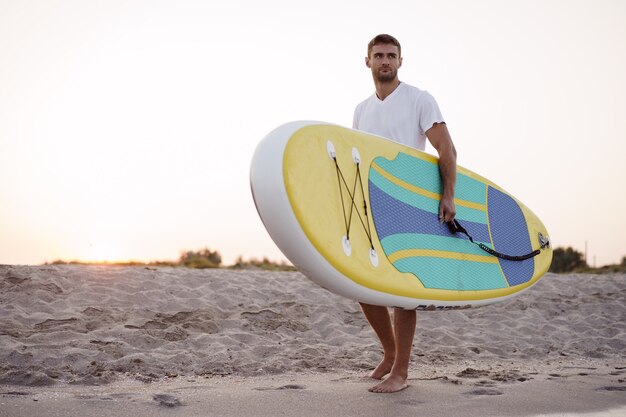 Giovane uomo che porta tavola da sup dopo la sessione di surf in acqua