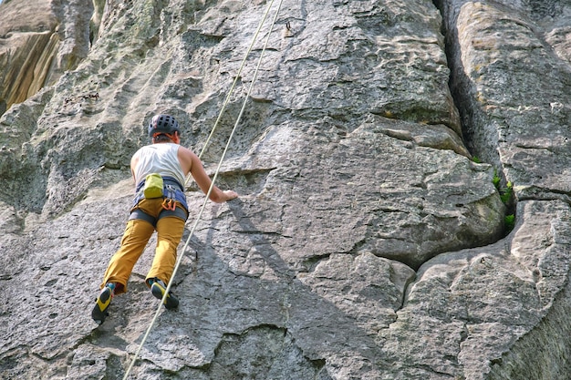 Giovane uomo che scala una parete ripida di una montagna rocciosa Lo scalatore maschio supera un percorso impegnativo Impegnandosi nel concetto di sport estremo