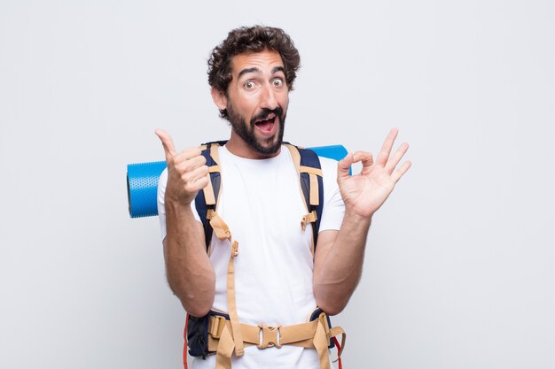 Giovane uomo che si sente felice, stupito, soddisfatto e sorpreso, mostrando i gesti ok e il pollice in alto, sorridente