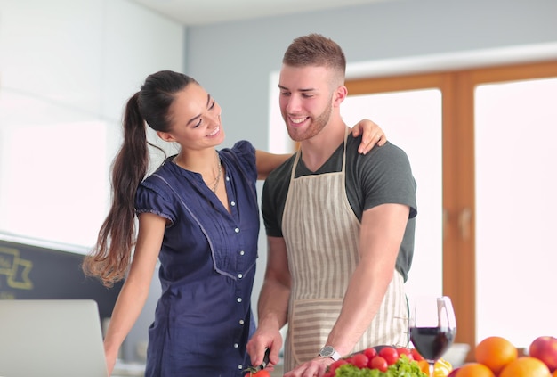 Giovane uomo che taglia le verdure e donna in piedi con il computer portatile in cucina