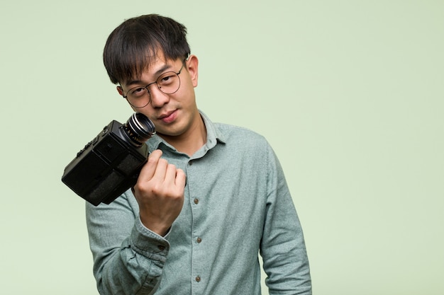 Giovane uomo cinese che tiene una macchina fotografica d'annata che invita a venire