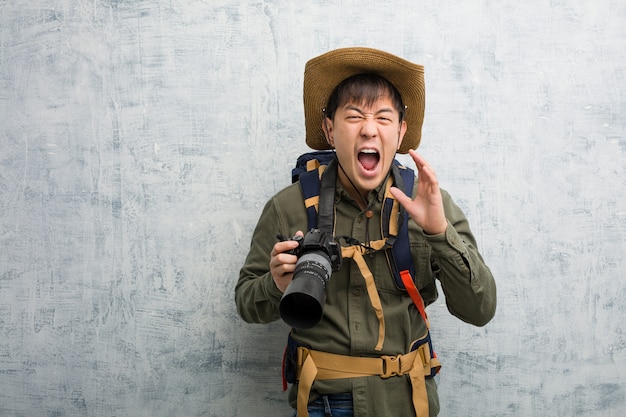 Giovane uomo cinese dell'esploratore che tiene una macchina fotografica che grida qualcosa di felice alla parte anteriore