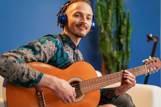 Giovane uomo con le cuffie seduto sul divano e suonare la chitarra