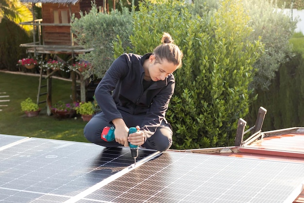 Giovane uomo concentrato di lavoro avvitando i pannelli solari al tetto con un cacciavite elettrico